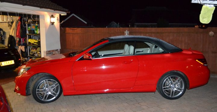 Show us your Mercedes! - Page 31 - Mercedes - PistonHeads - The image showcases a vibrant red sports car parked on a brick driveway. The car is a two-door convertible, with the top up, giving it a sleek and stylish appearance. The license plate on the car is partially visible. The driveway is situated in a residential area, as indicated by the fence and the light, which is presumably on the side of the house. The surrounding environment suggests a quiet and peaceful neighborhood during the night.