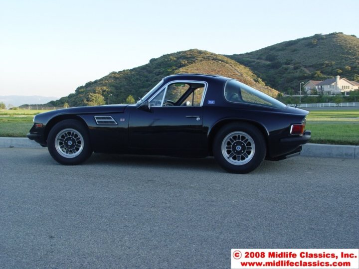 Early TVR Pictures - Page 80 - Classics - PistonHeads - The image features a classic car, possibly a Porsche, parked on a flat landscape during the daytime. The car is predominantly black with white and silver accents. It has a distinctive double buttress rear wing, which is a notable feature of Porsche models like the 911 and 917. The car is positioned on the left side of the road, with a clear view of a house situated on a hill in the distance, under a blue sky.