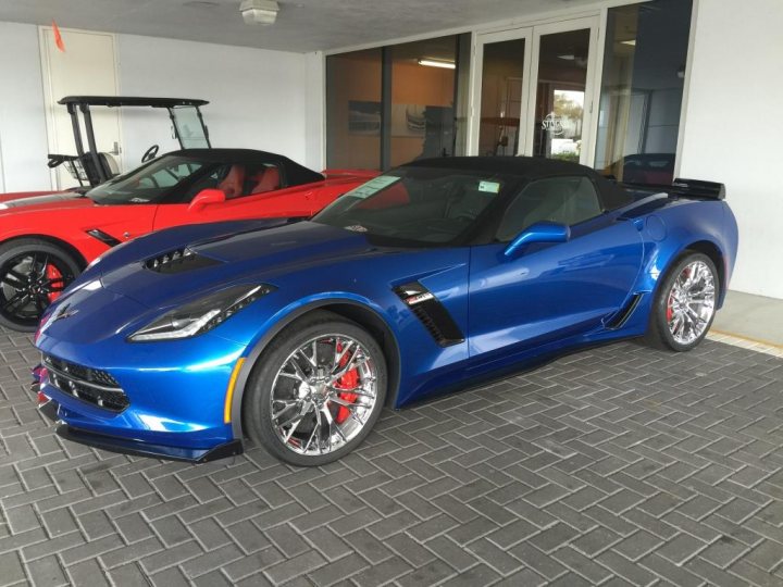 Daytona and Stingray Chevrolet (Z06). - Page 1 - Corvettes - PistonHeads - The image presents a comparison of two different correl cars in a showroom. The red car on the left is a convertible with a sleek design and black top, while the blue car on the right is a sports car with a solid roof. Both cars are equipped with black wheels and have visible slot emblems on the grille, indicating their brand. The showroom setting with its prominent large door and well-lit interior suggests a luxurious environment where these cars are displayed for potential buyers.