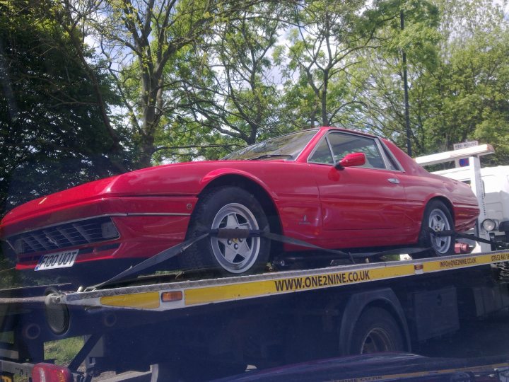 What on earth is this? - Page 1 - Ferrari V12 - PistonHeads - In the image, there's a vibrant red sports car being transported on a flatbed trailer. The sloped roof of the car adds to its stylish design. The trailer is parked under trees, suggesting that the scene might be outdoors. A text box on the trailer reads "www.one9nco.uk", indicating the towing company's website. The cars license plate is also visible.