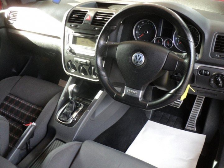 A close up of a car dashboard with a motorcycle - Pistonheads - The image displays the cockpit of a Volkswagen, showing the interior from a driver's side perspective. Features visible include the steering wheel, instrument cluster, center console, and the driver's seat. The car has a modern, sleek design with a central infotainment screen and digital gauges. The interior is upholstered in a grey cloth, and the sun is illuminating the scene.