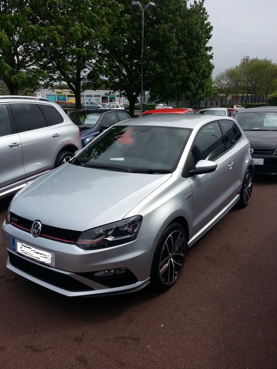 Polo GTI 2015 - Page 3 - Audi, VW, Seat & Skoda - PistonHeads - The image shows a single silver-colored car parked in what appears to be a parking lot. The vehicle features a sleek design with a prominent grille, black rims, and is equipped with a European-style license plate indicating its origin. In the background, there are other cars of various colors, suggesting a public parking area. The car's metallic finish reflects the lighting, giving it a shiny appearance.