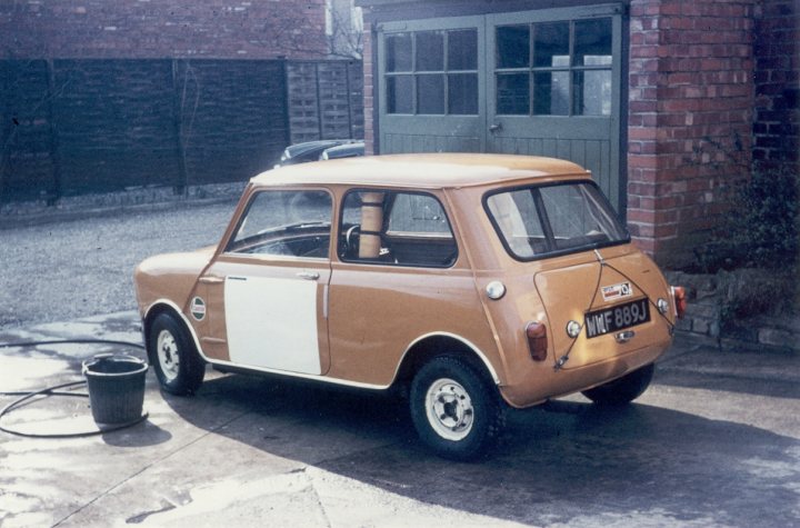 Classic Photos... - Page 1 - Classic Minis - PistonHeads - The image captures an orange Mini Cooper, parked neatly on a road with a brick building and a hedge visible in the background. The car is a classic model with the words "Morris Mini Cooper" written on it, suggesting it's a vintage model. The Mini Cooper, with its compact yet appealing design, stands out prominently against the backdrop, which may be an older part of town given the brick building and the hedge. The vehicle's position in the frame and the shadows cast on the ground confirm its location.