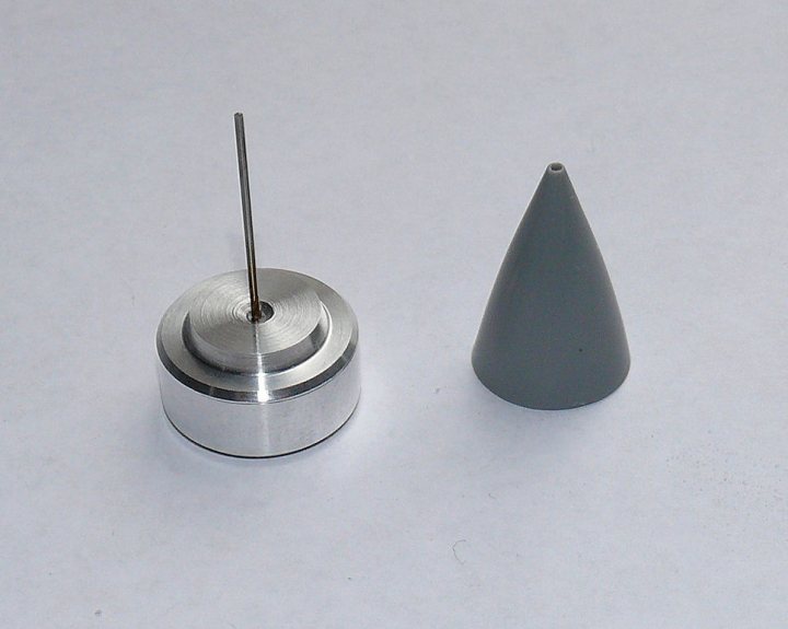 A pair of scissors sitting on top of a table - Pistonheads - The image displays two silver metallic pieces against a white background. The larger piece appears to be a hexagonal nut with a hole in the center where a bolt or screw might be inserted. The smaller object is a cone-shaped cap, the pointed end of which is positioned on top of the nut. The objects are centered and isolated, with no signs of connection or interaction between the two. The shiny surfaces suggest these are new and possibly made of stainless steel.