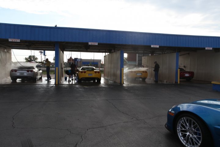 NCM Bash Pictures - Page 1 - Corvettes - PistonHeads - The image depicts an indoor parking garage. There are several cars visible, positioned on either side of the frame. Notable among the vehicles is a bright blue car parked closer to the foreground. The setting suggests a possible rainfall earlier, indicated by the wet ground. In the background, a person is visible near the cars' entrance/exit, appearing to be interacting with the cars. The overall lighting and shadows hint at an outdoor scene.