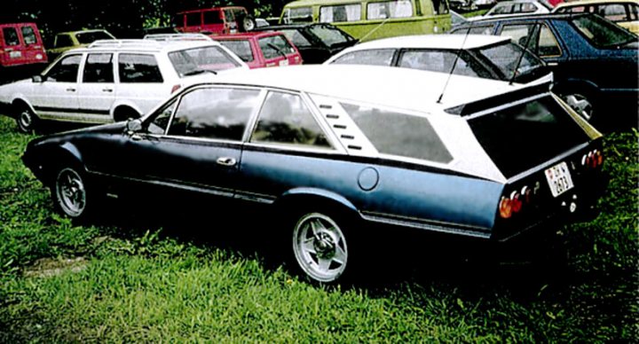 Ferrari Pistonheads Panther - The image features a selection of vintage cars parked on grass, presumably in a field or a classic car show. Among these vehicles stands out a blue and white vintage coupe with a hatchback, positioned towards the center of the frame. The car's unusual color scheme of royal blue fading into white at the rear and sides gives it a distinctive character. In the background, there's a line of various other vintage cars, their colors muted and blending into the outdoor setting. The scene suggests an event or gathering for classic car enthusiasts.