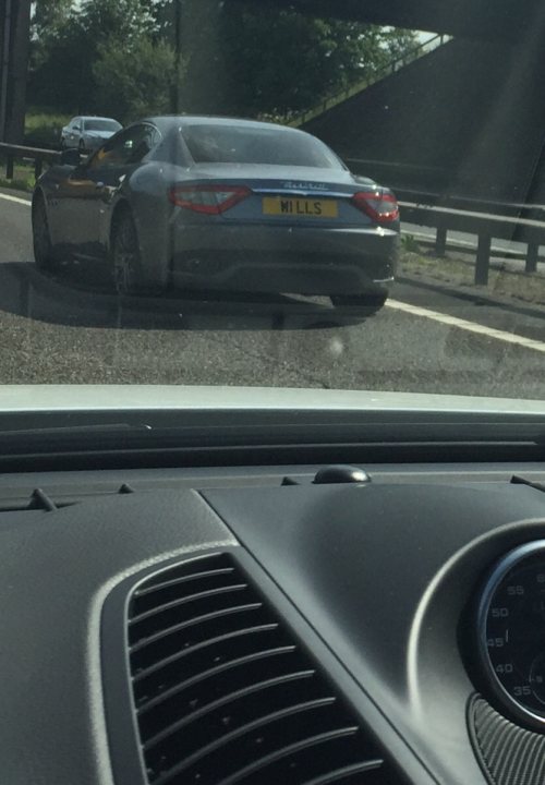 Real Good Number Plates : Vol 4 - Page 348 - General Gassing - PistonHeads - The image captures a moment on a highway, as seen through the windshield of another moving vehicle. The focus is on a gray luxury car, smooth and polished, with the distinctive taillights of a Porsche. The car is traveling under a large overpass, suggesting the presence of an elevated road or structure nearby. The perspective is from behind, offering a rear view of the vehicle and its license plate, which reads "Will's".