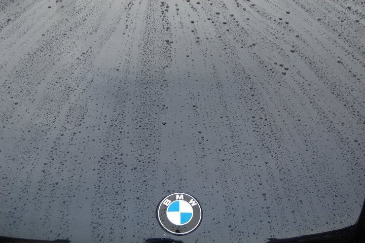 Lucky Luciano detailed my motor! - Page 1 - South West - PistonHeads - The image captures the view through an opened automotive hatchback. The sky outside is gray and cloudy, with droplets of rain visible on the car's window. The glass window is embellished with a logo of BMW, a renowned car manufacturer. The daylight is partly obscured by the thick raindrops, giving the picture a dramatic effect. The rain adds a unique texture to the scene.