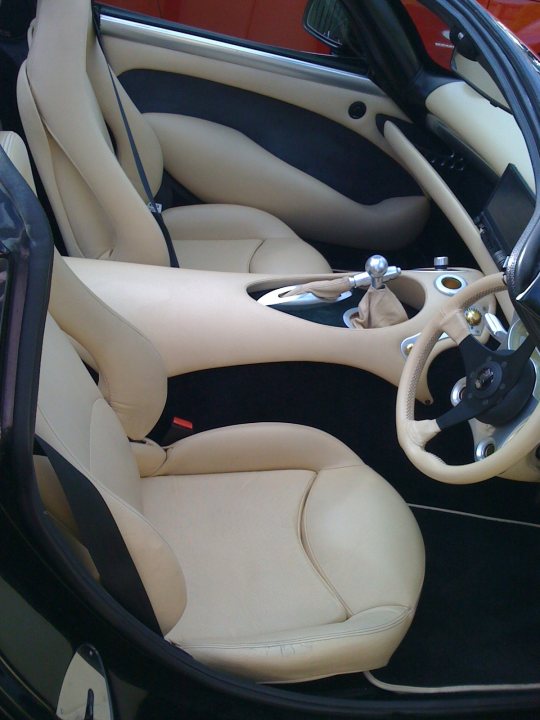 Pistonheads - This is a photograph of the interior of a luxury car with a visible dashboard, steering wheel, and driver's seat. The car is predominantly white with beige leather upholstery, and the surfaces exhibit a reflective quality, as is common in car interiors, indicating technical details like gauges, controls, and side-view mirrors are visible. The photo captures the car's interior from the perspective of a viewer seated in the passenger seat, showing the curvature of the doors and the spaciousness of the cabin. The sunlight is coming in through the windows, with the reflection visible on the car's dashboard, further highlighting the car's sophisticated design.