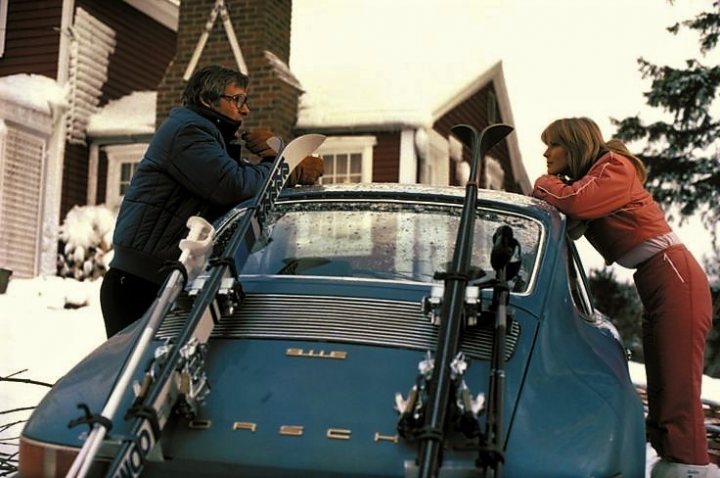 A few pictures I quite like - please add to it ...... - Page 6 - Porsche General - PistonHeads - In the image, we see a man and a woman. They are both bending over a naval blue car, which is parked at an angle. The skis on the car suggest that they might be preparing to go skiing. The car is covered in a thick layer of snow, indicating a wintry setting. The house in the background seems to be a traditional red-brick house, enhancing the overall winter scene.