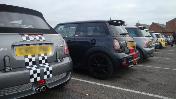 Pistonheads Oxford Sunday Service - The image shows a parking lot filled with cars. Specifically, a sequence of small cars is parked. Some cars have unique checkered patterns on their bodies, while others have more traditional solid colors. There is no visible activity within the parking lot; the cars are parked orderly beside each other. The setting appears to be on a cloudy day.