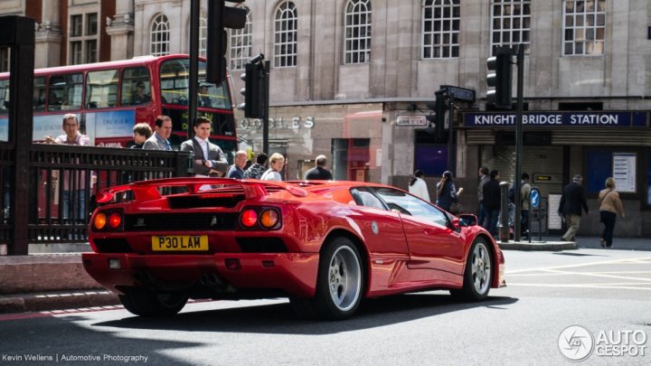 V12 Lambo Photo Thread - Page 3 - Diablo/Murcielago/Aventador - PistonHeads - In the image, a vibrant red Ferrari is captured in motion on a city street, with a splash of color illuminated by sunlight. The car is located in the foreground of the image, drawing attention to its unique design and striking hue. It's crossed the Knight Bridge, as indicated by the sign in its background. 

People are seen walking on a sidewalk next to a red double-decker bus, which suggests a lively, bustling area of the city. The presence of other pedestrians and cars in the scene also contribute to the urban atmosphere. The image captures a moment of dynamic city life, with the Ferrari as a symbol of luxury and speed.