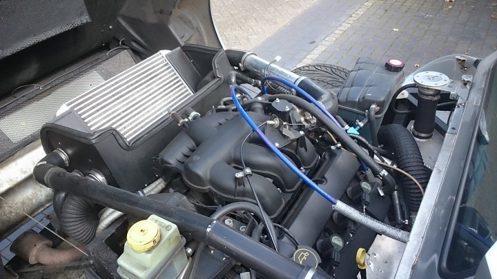 A close up of a motorcycle parked on a street - Pistonheads - The image shows a close-up view of an engine compartment of a vehicle. At the center of the image, there is the engine with various metal components. On the floor of the car, a rear tire is visible, and there are a few parts scattered on the side of the engine. The picture also captures the gray interior of the vehicle.