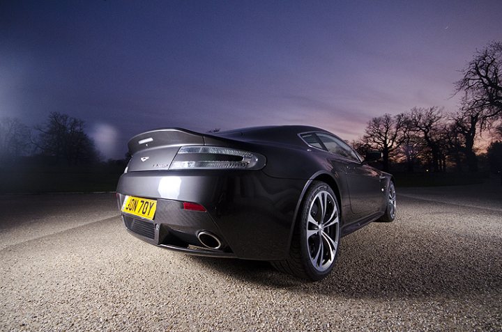 Pistonheads - The image captures a luxurious sports car at night, parked on what appears to be gravel or a soft dirt surface. The car, with its sleek design and shine from its headlights and tail lights, is the focal point of the image, designed with a large spoiler and a distinctive license plate that reads "JOY." The car's reflection can be seen on the surface beneath it, adding an interesting visual element. The background is a dark sky, suggesting it is nighttime, and in the distance, there's a silhouette of a tree, providing a natural contrast to the man-made machinery in the foreground.