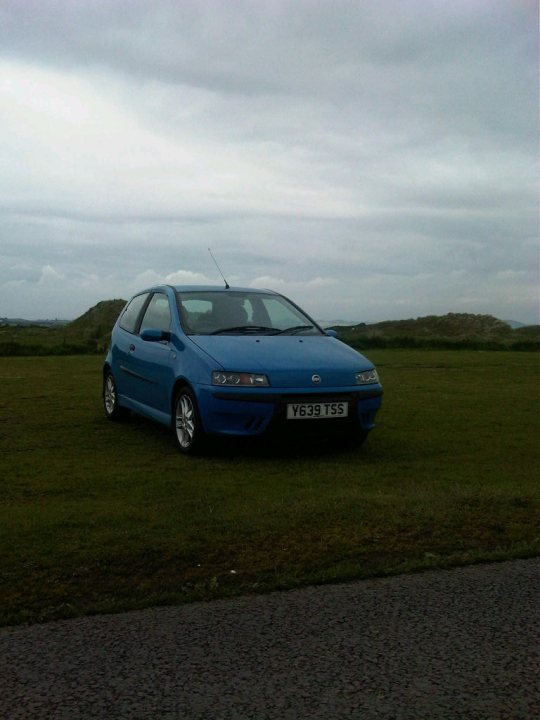 New Toy  - Page 1 - Readers' Cars - PistonHeads - The image shows a vivid blue hatchback car parked on a grassy field. The sky overhead is overcast, giving the scene a somewhat moody atmosphere. The car appears to have a European license plate style, which suggests it might be a European model. The license plate is prominently displayed in the front of the car, indicating possibly the car's identity or ownership. The car's bright blue color stands out against the more muted tones of the landscape.