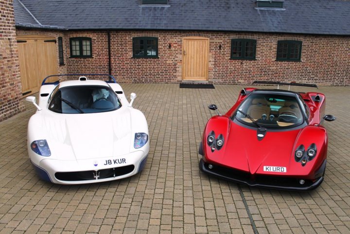 Factory Grigio Titanio Enzo at DK Engineering - Page 1 - Supercar General - PistonHeads - The image showcases a scene of two luxury sports cars, a white one and a vibrant red one, parked side by side on a brick driveway. The white car is positioned towards the left side of the frame, while the red car is on the right. Both cars are facing the same direction, possibly towards a building located in the background, suggesting the image might have been taken at a residence or business facility.