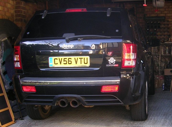 Where's your smiley? - Page 1 - Kent & Essex - PistonHeads - The image shows a black SUV parked in a garage. The license plate of the vehicle reads "C7 V Port". It's a Jeep brand vehicle, as indicated by the manufacturer's logo visible on the trunk. The side mirror and rear light are illuminated, suggesting that the vehicle's lights are on. The garage appears to be filled with other vehicles, indicating a full garage space.