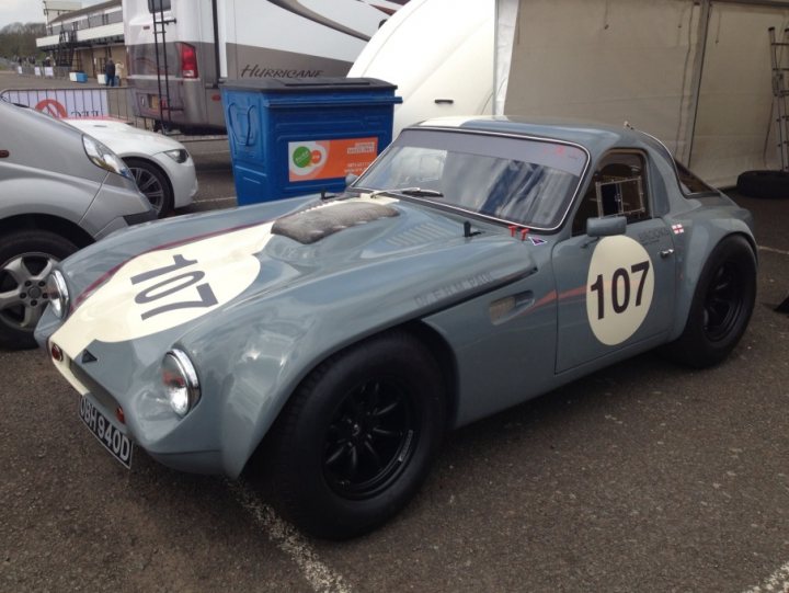 Early TVR Pictures - Page 32 - Classics - PistonHeads - The image shows a grey race car with a white top parked on an outdoor lot. On the side of the car, the number "107" is prominently displayed. In the background, there are several vehicles, including a motorhome and a white car. To the right of the motorhome, there is a blue trash bin. The overall mood of the image is exuberant, suggesting a lively race event.