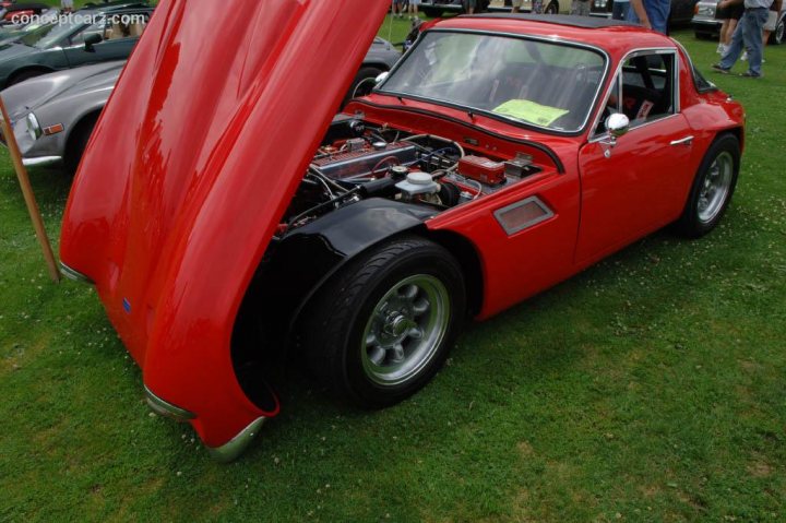 Early TVR Pictures - Page 72 - Classics - PistonHeads - The image features a red vintage sports car with an open hood, allowing a view of its engine. The car is parked on a grassy area, with other vehicles and people in the background, suggesting a gathering or event. The vintage appeal of the car is highlighted by its glossy red body and the visible mechanical components under the hood. The vehicle appears well-maintained and cared for, as indicated by its clean and polished condition.