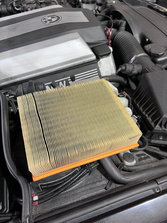 E31 840Ci - first ever BMW (and a daily!) - Page 7 - Readers' Cars - PistonHeads UK - The image shows a close-up view of an automobile engine. A car air filter is prominently displayed in the foreground, attached to the engine. This part has multiple layers and appears to be made from metal mesh with cardboard filters on top. Behind the filter, we can see the complexities of the engine, with various wires, tubes, and mechanical components visible, suggesting it's a complex piece of machinery. The overall image is in black and white, highlighting the textures and patterns within the engine.