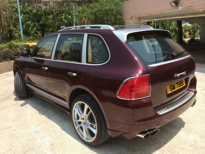 Porsche cayenne 4.5 or 4.5 turbo which one - Page 1 - Front Engined Porsches - PistonHeads - The image presents a maroon-colored SUV which appears to be a model by the brand Audi. The car parked on a driveway is positioned diagonally, showcasing its red taillights and a spare tire. The license plate of the vehicle is clearly visible. In the background, there are palm trees and what seems to be a building, suggesting this could be a location in a tropical or subtropical region. The photo is taken during daylight, and the driveway is dry, indicating no recent rain.