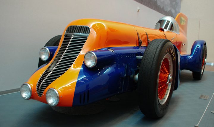 Fantastic Motorsport Photos! - Page 198 - General Motorsport - PistonHeads - The image features a vibrant blue and orange vintage racing car, which is the prominent subject of the photograph. The car is parked indoors, possibly in a museum or exhibit, as indicated by a painted backdrop. The driver's seat is visible, suggesting that the vehicle may be occasionally open for visitors to explore. The design and color scheme of the car suggest that it hails from an earlier era of automotive history.