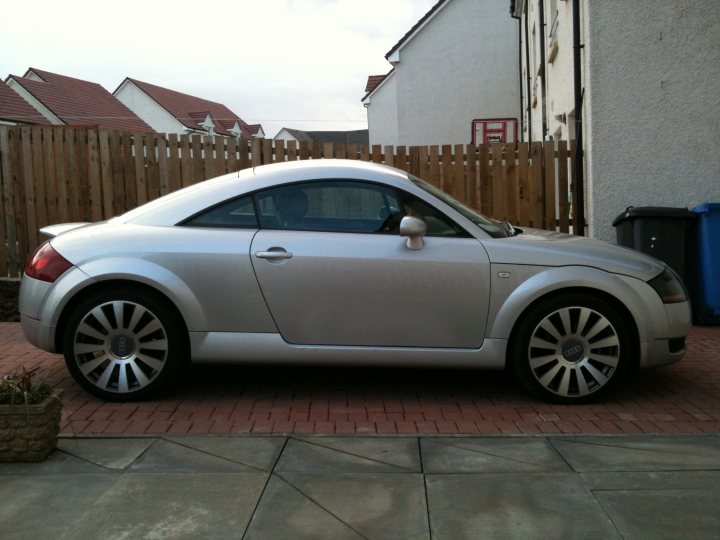 Our Cars - Page 40 - Scotland - PistonHeads - The image showcases a silver sports car parked on a sidewalk adjacent to a row of brown townhouses. The car is positioned at an odd angle to the curb, with one of its rear wheels visible. In the background, there is a wooden fence and a garbage can is visible among the houses.