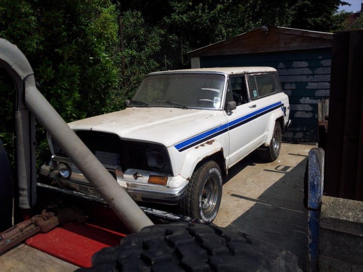 (introduction) My name is Tim and i have an addiction. - Page 1 - Off Road - PistonHeads - The image showcases a vintage hatchback parked in front of a garage. The car, with its distinctive blue stripe running down the side, appears to be in a state of disrepair or perhaps being restored. It's loaded down with one large metal object that looks like a tailgate accessory, and it's secured with a red strap, suggesting it has been recently loaded or unloaded. The garage provides a backdrop for the scene, and there's a sense of anticipation, perhaps for a journey or simply for the completion of the car's restoration.