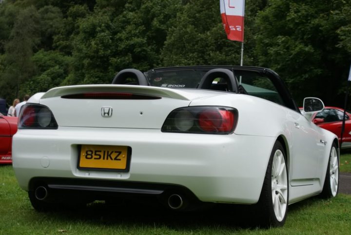 Pistonheads - This is a color photograph of a white Honda sports car parked among other vehicles in a grassy area with trees visible in the background. The car's body features a sleek design with a black rear spoiler, and the license plate reads "85IK2Z". The vehicle is positioned at an angle to the camera, revealing the front and side profile. The image captures an outdoor setting, possibly during an event or a gathering of car enthusiasts.