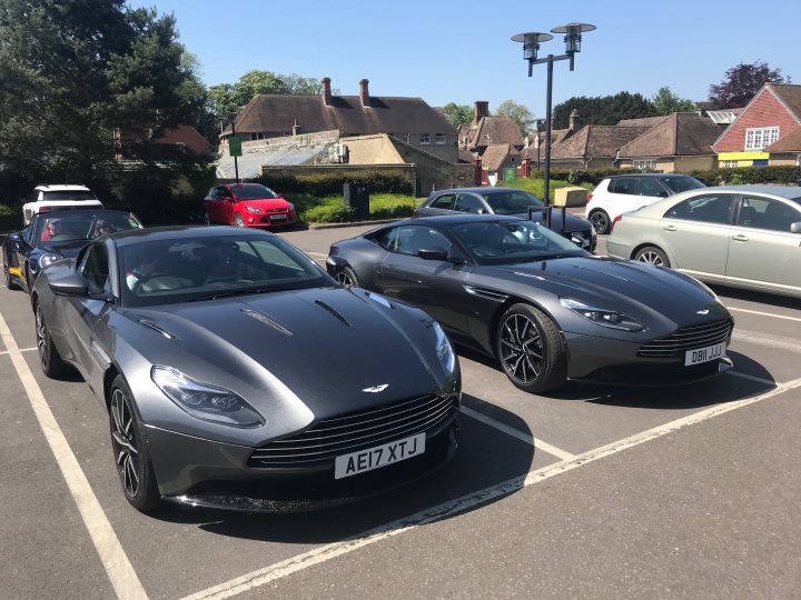 DB11 Snap! - Page 1 - Aston Martin - PistonHeads - In this image, two sports cars are prominently displayed in a parking lot. One of the cars is a sleek silver Aston Martin, while the other is a fast black Aston Martin. The cars are parked side by side, adjacent to each other. They are positioned along a white line that runs through the parking lot, indicating a designated parking area for certain types of vehicles. In the background, there are several other cars parked, but they are not as noticeable as the two sports cars.