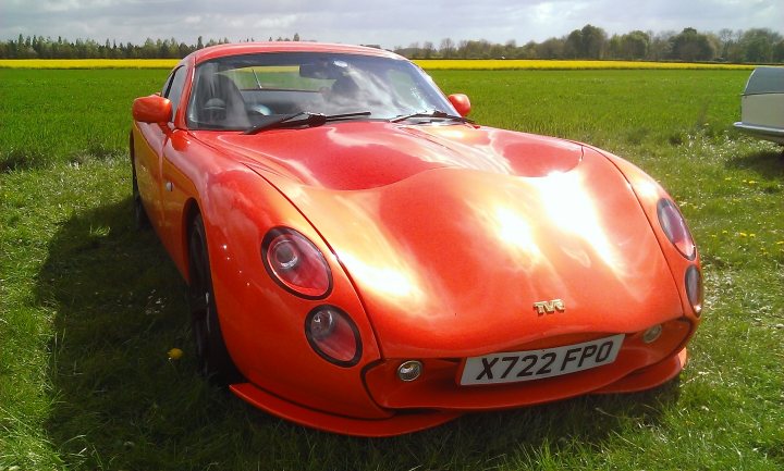 Your Best Tuscan Pic... - Page 27 - Tuscan - PistonHeads - The image showcases a vibrant orange sports car parked in a lush green field, creating a striking contrast. The car appears to be a vintage model based on its design and color. There are four tires visible in the frame, two at the front and two at the back of the car. The engine hood is prominently visible, displaying the model name in gold. In the backdrop, there's a hint of agricultural activity, suggesting the field might be a farm. The overall setting and the car itself evoke a sense of nostalgia and excitement for vintage automotive enthusiasts.