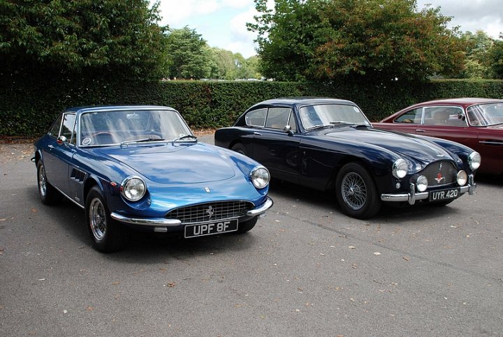 GRRC Lunch Club - Page 1 - Goodwood Events - PistonHeads - The image features two classic sports cars parked on a paved surface in what appears to be a park or a similar open and green space with trees in the background. The blue car, which appears to be a convertible with a adjustable top, is parked on the left side of the image while the black car, also a convertible, is parked on the right side. Both cars show some wear and tear, suggesting they are well cared for but have seen some use over the years. There is a clear sky visible in the upper part of the image, with a few clouds on the horizon. The overall scene evokes a sense of nostalgia and appreciation for vintage automobiles.