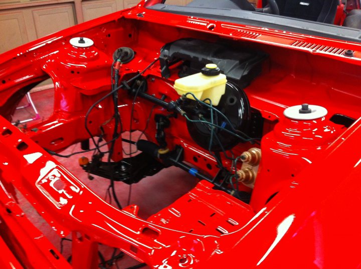 Pistonheads - The image shows an open car hood revealing the red interior of a vehicle. The car appears to be in the process of being worked on or restored, indicated by the visible wires and mechanical parts. The engine is one of the components visible, housed beneath the red plastic coverings within the engine bay. The image captures the complexity and industrial aesthetic of the vehicle's undercarriage.