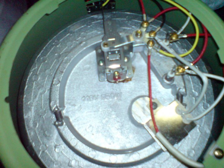 A close up of a bike with a helmet on it - The image shows an intricate electronics circuit inside a green enclosure. An insulator separates the wires, and connections are made using red and yellow wires. There's a cord wrapped around a black knob, likely for volume or other adjustments. Metallic components, including a key-like object, suggest this could be a component of a fuse box or similar electric setup. The circuitry is well-organized, with various parts arranged around a central black object, which could be a battery or another source of power.