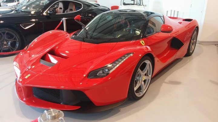 A close up of a red and black motorcycle - Pistonheads - This image captures an indoor scene featuring two luxury sports cars. On the left, a sleek black car is parked, its polished surface reflecting light from the space. On the right, a vibrant red sports car steals the show. It's equipped with distinctive features such as the golden grille,spotted side mirrors, and twin tailpipes, all highlighting its aggressive design. The red car's seat is visible through the glass roof, adding to its allure. The relative positions of the cars and the open doors suggest a showroom setting, possibly preparing for an event or a drive.