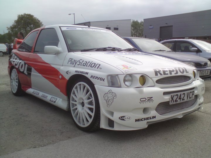 Pistonheads - The image shows a customized sport car. It is predominantly white with red accents and a black stripe. The front of the car prominently features a PlayStation logo and other stickers. The car is equipped with a spoiler, blacked-out wheels, and aduil lights, giving it a unique and modified look. The car appears to be parked near other vehicles in what seems to be a parking lot.