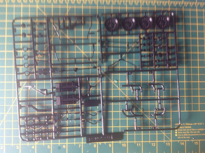 Fujima Alfa Romeo T33 stradale - picture heavy (possibly) - Page 1 - Scale Models - PistonHeads - The image shows an intricate assembly of metal components and fastenings laid out on a green ruler. The components are likely part of a kit, possibly for a mechanical model or a model vehicle. The pieces appear to be small in size, with a combination of larger and smaller parts that are designed to fit together to create a larger structure. The metallic parts are clean and shiny, indicating that they are either new or well-maintained. The presence of the yellow grid superimposed over the ruler suggests a building or construction context.