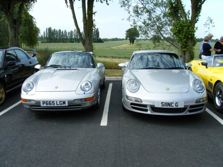 Breakfast Meeting, The Hare, Roxwell 4th June - Page 1 - Kent & Essex - PistonHeads - The image shows a two-car parking space with two Porsche convertibles positioned side by side. The vehicles feature two different license plate designs, which look like "PG65 LGM" and "SINC G". They are both metallic, reflecting the sky, with a classic convertible design, and they are parked facing the same direction. In the background, there is a grassy field that suggests a rural setting, and to the right, there are some trees and people standing at a distance, possibly observing the cars.