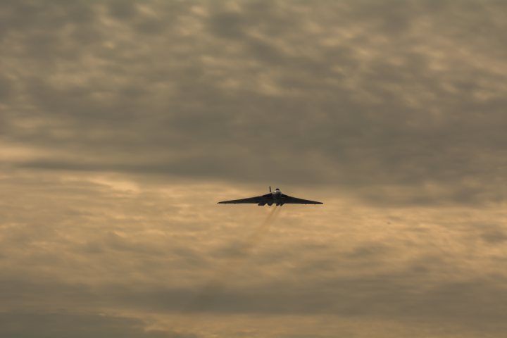 XH558.......... - Page 297 - Boats, Planes & Trains - PistonHeads - The image captures a moment of a solitary fighter jet soaring against a backdrop of a cloudy sky. The jet is flying at a high altitude, creating a small, almost insignificant profile against the expansive canvas of the sky. The color palette of the image is dominated by earthy tones, with the sky appearing a blend of brown and grey, and the jet maintaining a stark black silhouette. The plane is depicted with exhaust fumes trailing from its rear, indicating its active flight state. The overall composition of the image suggests motion and power, synonymous with the image of the jet, seemingly on a mission amidst the brooding clouds.