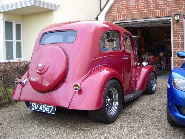 Lets see a picture of your classic(s) - Page 86 - Classic Cars and Yesterday's Heroes - PistonHeads - The image shows a vintage red car parked in a garaged setting. The vehicle is a convertible, with the top up revealing a red interior with visible stitching. The car is positioned at a slight angle to the camera, highlighting its classic design. Surrounding the car, the garage interior features various items on display, such as bottles and objects on shelves, indicating a space that is both functional and perhaps decorative. The style of the car, especially noticeable from the rear, suggests it's a classic model, possibly from the early to mid-20th century.