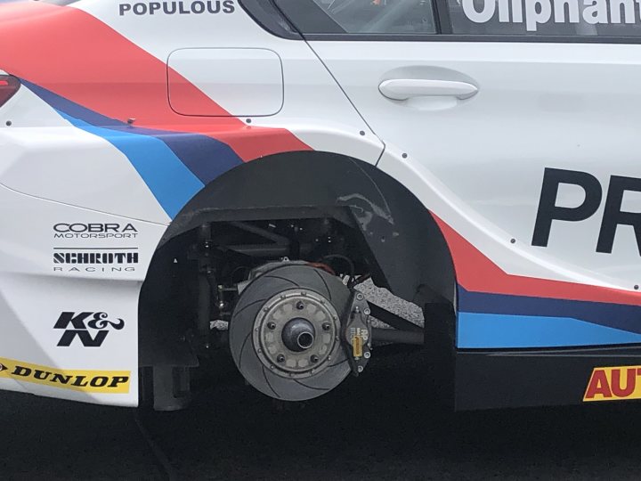 M135i Track build with a hint of BTCC - Page 4 - Readers' Cars - PistonHeads - The image shows a close-up view of the rear wheel and suspension of a BMW race car. The car is adorned with various sponsors' logos, including 'Populist', 'K&N', 'Autobahn', and 'Cobra'. It has a white color scheme with blue and red accents that resemble the colors of the British flag. The wheel is fitted with stickers on the rim. The car's license plate is visible but not legible in the image. The tires have a prominent tread pattern, indicating they are designed for performance or racing purposes. The suspension components are clearly visible, revealing the complexities of modern race cars.