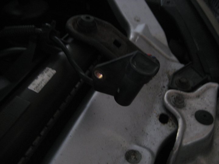 A close up of a pair of scissors - Pistonheads - The image captures a close-up view of an automotive component, which appears to be a metal electromagnetic coil. This coil is connected to a black connector that has a red LED light inside. The coil is held in place with a white retaining clip. This mechanical assembly is mounted under the car's loose lid, as indicated by the lighting illuminating the scene.