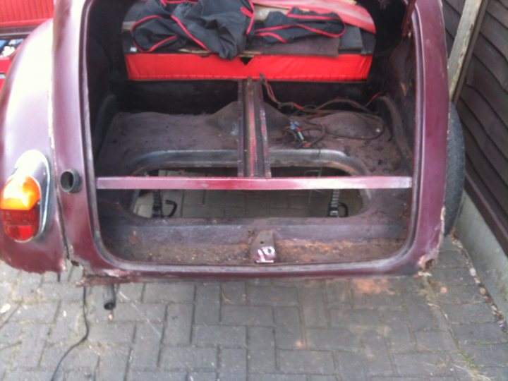 1971 Morris Minor 1000 Resto thread (Maybe) - Page 1 - Classic Cars and Yesterday's Heroes - PistonHeads - The image depicts a vintage car, specifically focusing on its trunk area. The trunk lid is open, revealing a red blanket and a pair of red luggage secured at the back. Inside the car, the backseat area can be seen with a red cloth folded neatly. The interior of the car appears to have white roof filters. The car is comfortably parked on a resurfaced driveway.