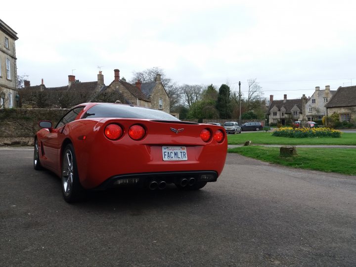 RE: PH Service History: Hyper milers? - Page 3 - General Gassing - PistonHeads - The image features a vibrant red Corvette that has just pulled into the driveway of a large country house. The car, with its Chrome Tailpipe, is facing the left side of the image. The landscape is picturesque, with the buildings made of stone and topped with pointed roofs. The car is near a well-maintained flower garden, hinting at the attention to detail by the house owners. The sky is overcast, suggesting it might be a cool or cloudy day.