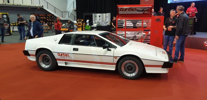 RE: Lotus Turbo Esprit | Spotted - Page 1 - General Gassing - PistonHeads - The image shows a car show event with a vintage sports car on display. This specific vehicle is an Audi Quattro, identifiable by the distinctive "Audi" emblem and its rally-inspired design. It's parked in front of a stage where there are a few attendees who appear to be enthusiasts or possibly judges at this event. The setting seems to be indoors, as suggested by the artificial lighting and the controlled environment. The Audi Quattro is likely the centerpiece or one of several highlights of this car show.