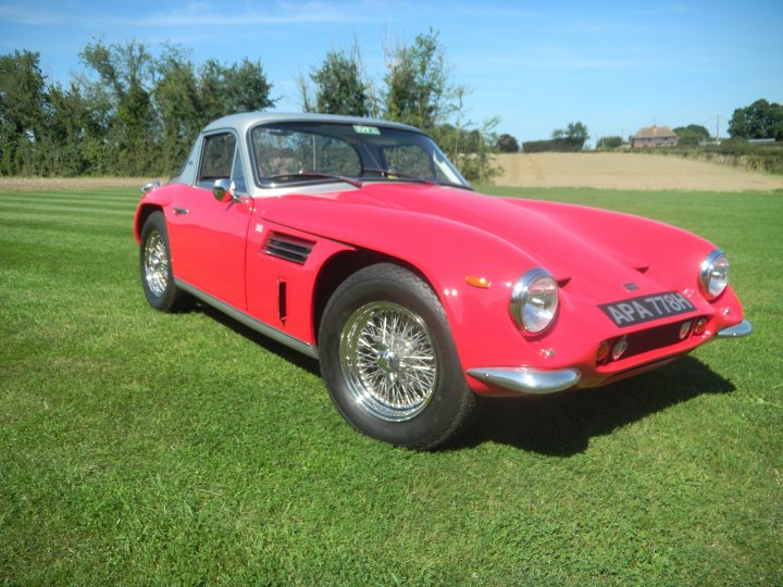 Lets see a picture of your classic(s) - Page 279 - Classic Cars and Yesterday's Heroes - PistonHeads - The image features a striking red sports car, dappled with a black roof and sporty black wheels. The car is parked amidst a lush green field, with the sensation of speed emphasized by the motion blur effect. The backdrop is made up of a clear blue sky, dotted with a few clouds, and it's a bright day, possibly a sunny afternoon. The tranquility of the rural setting contrasts with the sleek, angular design of the sports car, creating a visually appealing juxtaposition.