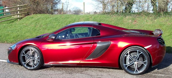 Deed Done! - Page 1 - McLaren - PistonHeads - The image portrays a vibrant red McLaren car parked on a road. The car's sleek design and aerodynamic body suggest speed and performance. The background features a grassy area, providing a natural contrast to the car's urban delight. A fence can be seen in the distance, indicating the proximity of the road to residential or pastoral lands. A lone tree stands in the background, adding to the overall aesthetic of the scene.