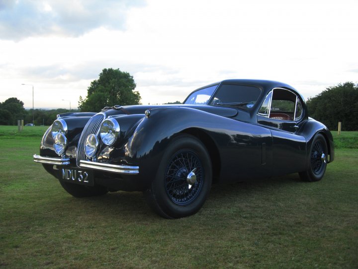 Pistonheads - This image showcases a classic car, possibly a Bentley given its distinctive design, as it's parked on a grassy area of a farm or similar rural setting. The vehicle is predominantly blue, and it features a front grille and two headlights. The sunlight casts a slight shadow on the car, adding depth to the scene.