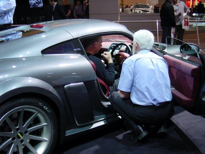 Pistonheads - The image portrays a scene inside a car show. A group of people, possibly a couple, are engrossed in examining the interior of a convertible sports car. The car itself is a striking mix of silver and pink, with a shiny interior that offers a contrasting seat's material for comfort. The two men, both dressed appropriately for the occasion, stand close to each other, suggesting a shared interest in the vehicle. The event appears to be bustling, with other people in the background, indicating that this might be a specific section dedicated to convertibles or luxury vehicles within the larger car show.