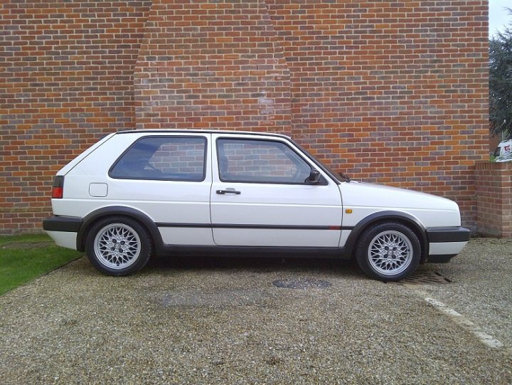 New toy :D - Page 1 - East Anglia - PistonHeads - The image showcases a white Volkswagen Golf car parked in front of a red brick building. The car has black wheel trim and is positioned slightly to the left from the camera's perspective. It's parked on a asphalt surface with a grey rocky area to its right.